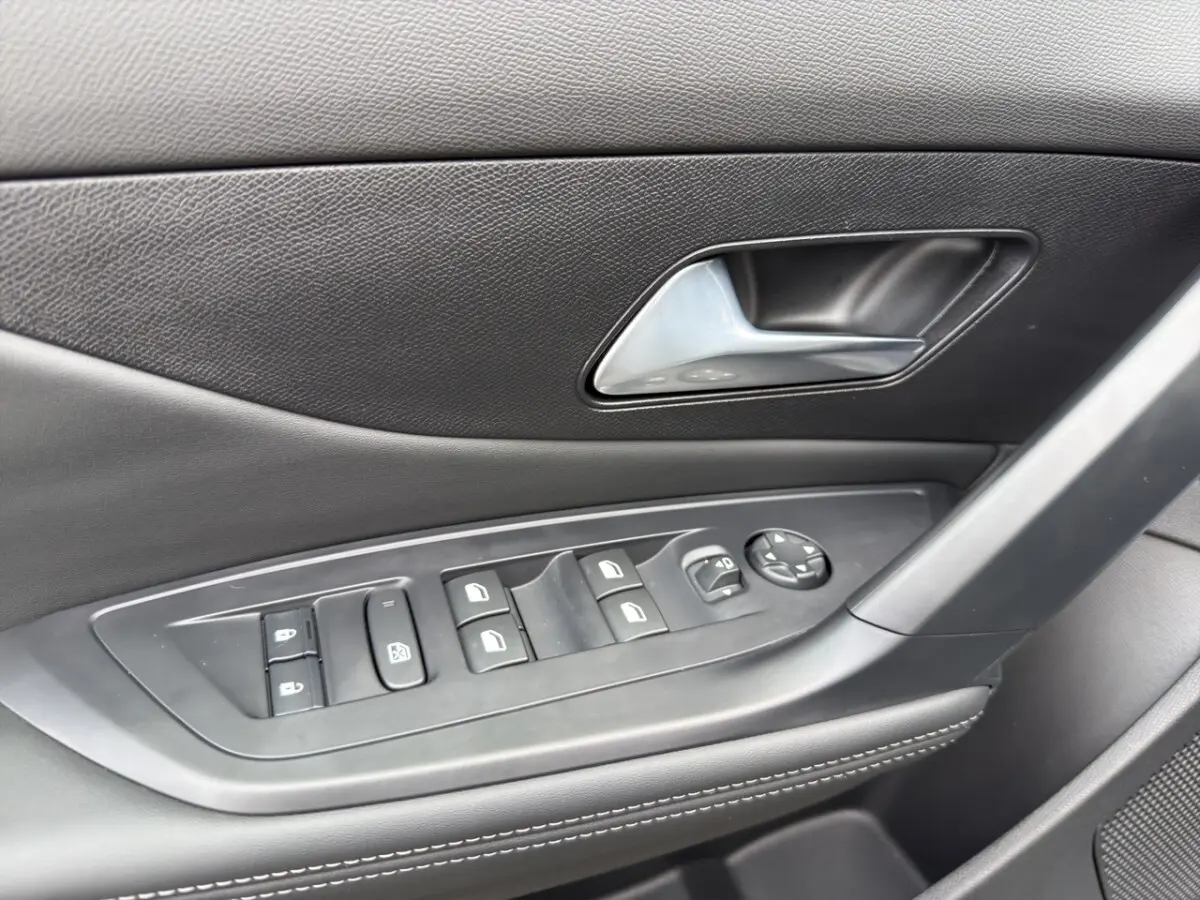 Gros plan sur la commande des vitres et rétroviseurs côté conducteur de la Peugeot 308 Hybrid gris foncé, intérieur noir.