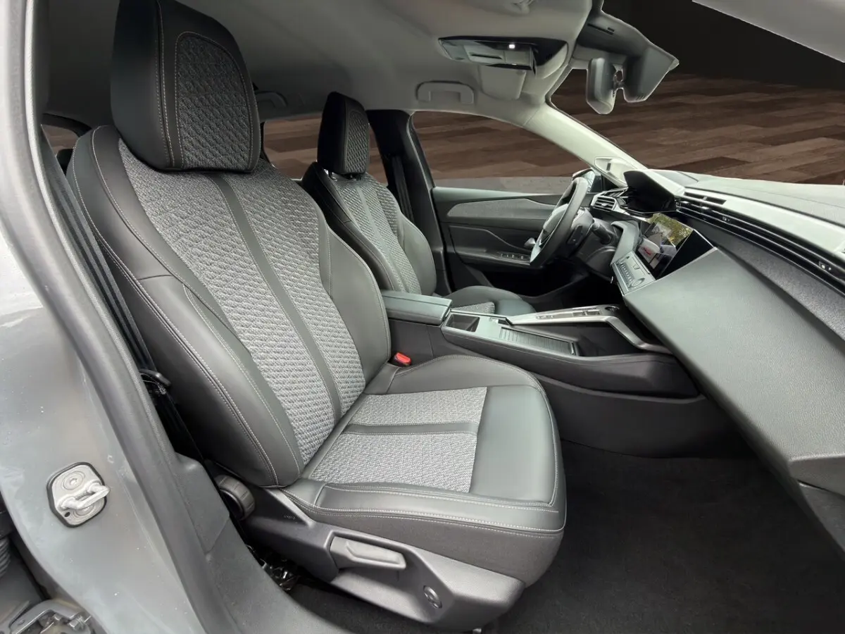 Vue intérieure côté conducteur de la Peugeot 308 Hybrid 145 e-DCS6 Allure 2025 avec sièges gris cuir et tissu, tableau de bord moderne.
