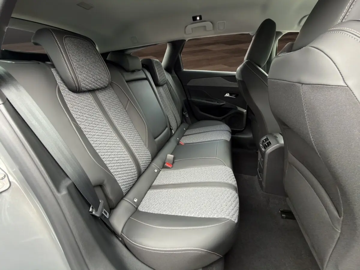 Vue intérieure arrière côté droit de la Peugeot 308 Hybrid 145 e-DCS6 Allure avec sièges gris foncé bi-matière et ceinture de sécurité.