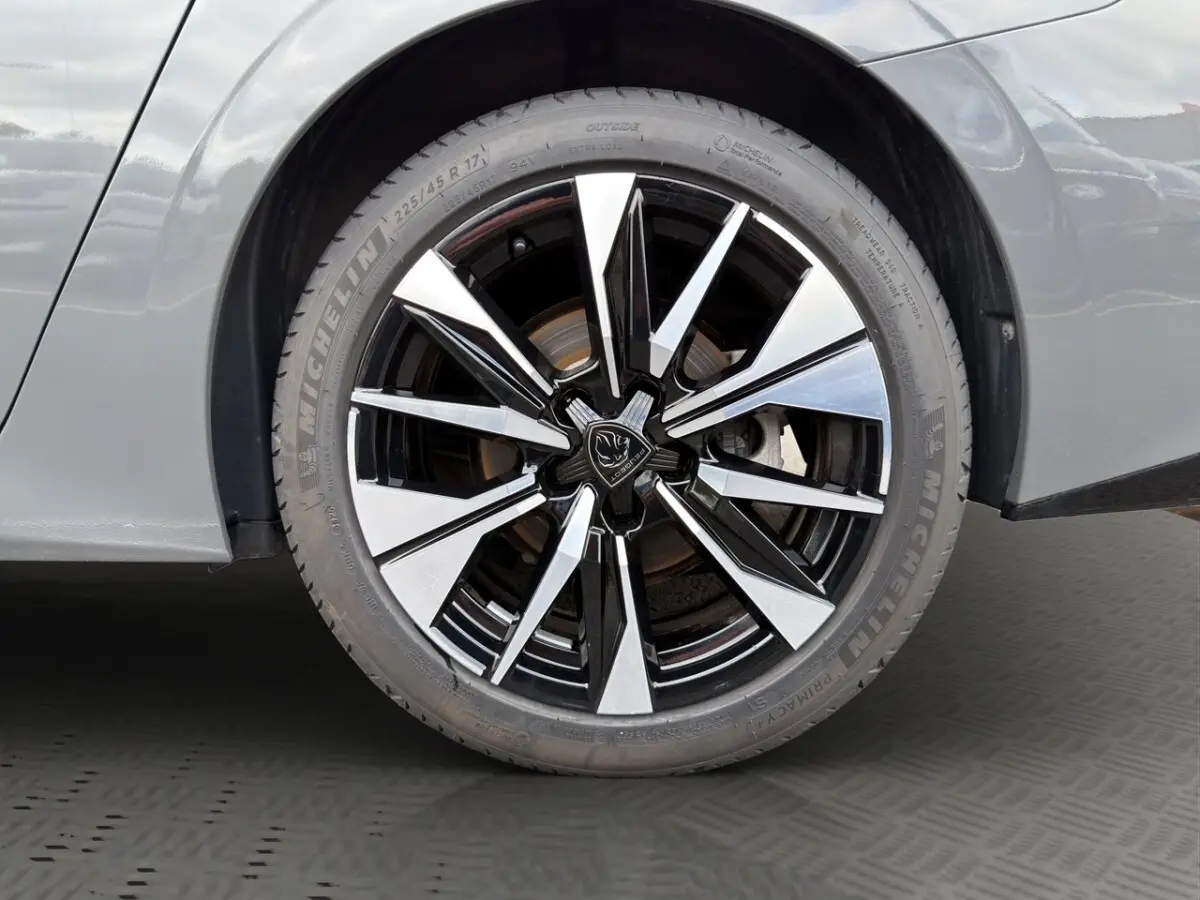 Gros plan sur la roue avant gauche de la Peugeot 308 Hybrid 145 e-DCS6 Allure gris foncé avec jante alliage bicolore.