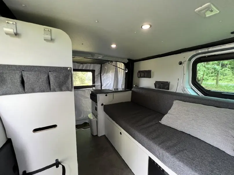 Intérieur du Renault Trafic Fourgon aménagé, vue latérale droite, banquette grise et rangements blancs lumineux.