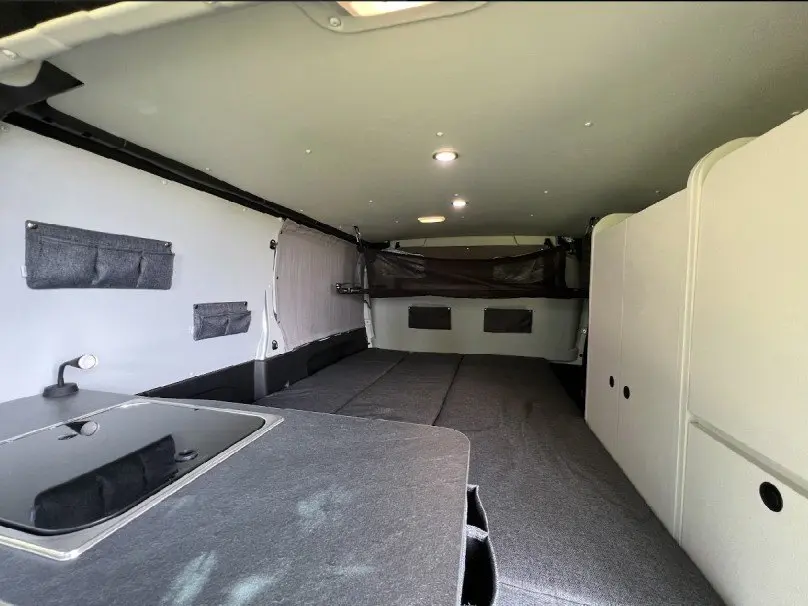 Vue intérieure arrière du Renault Trafic Fourgon aménagé Antilope Flex 3, avec couchage gris et rangements blancs.