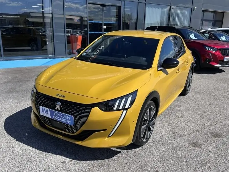 Peugeot 208 jaune faro vue 3/4 avant droit, avec calandre noire et feux LED distinctifs, stationnée devant un showroom.