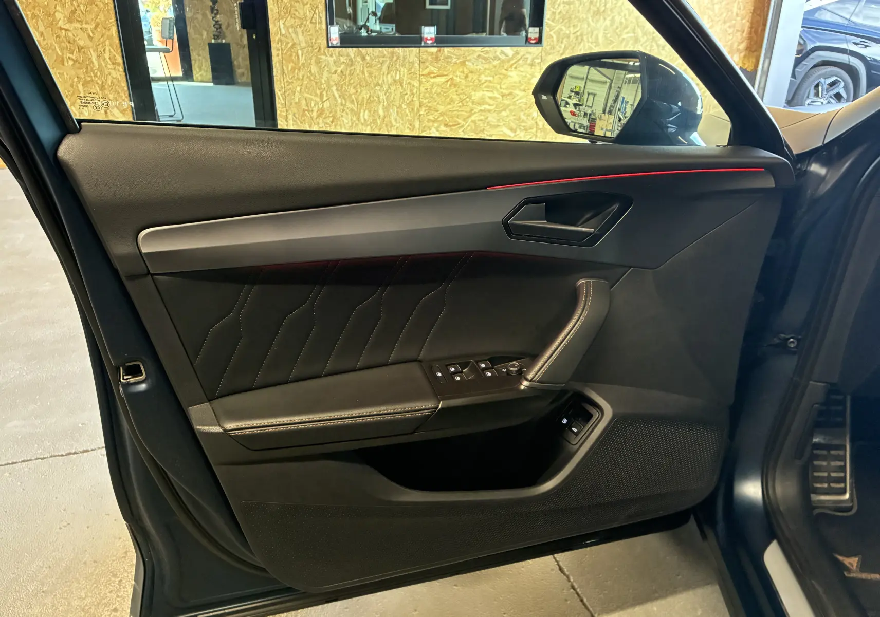 Vue intérieure de la porte avant gauche bleu nuit du CUPRA Formentor avec surpiqûres et bandeau rouge lumineux.