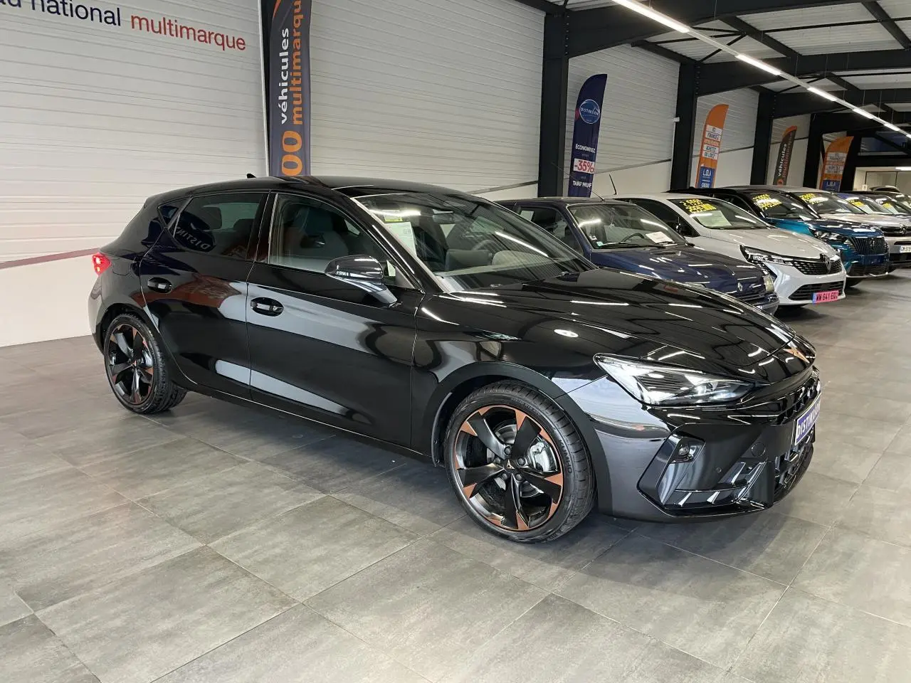 Vue 3/4 avant droite d'une CUPRA Leon noire avec jantes alliage 18'' cuivrées dans un showroom.
