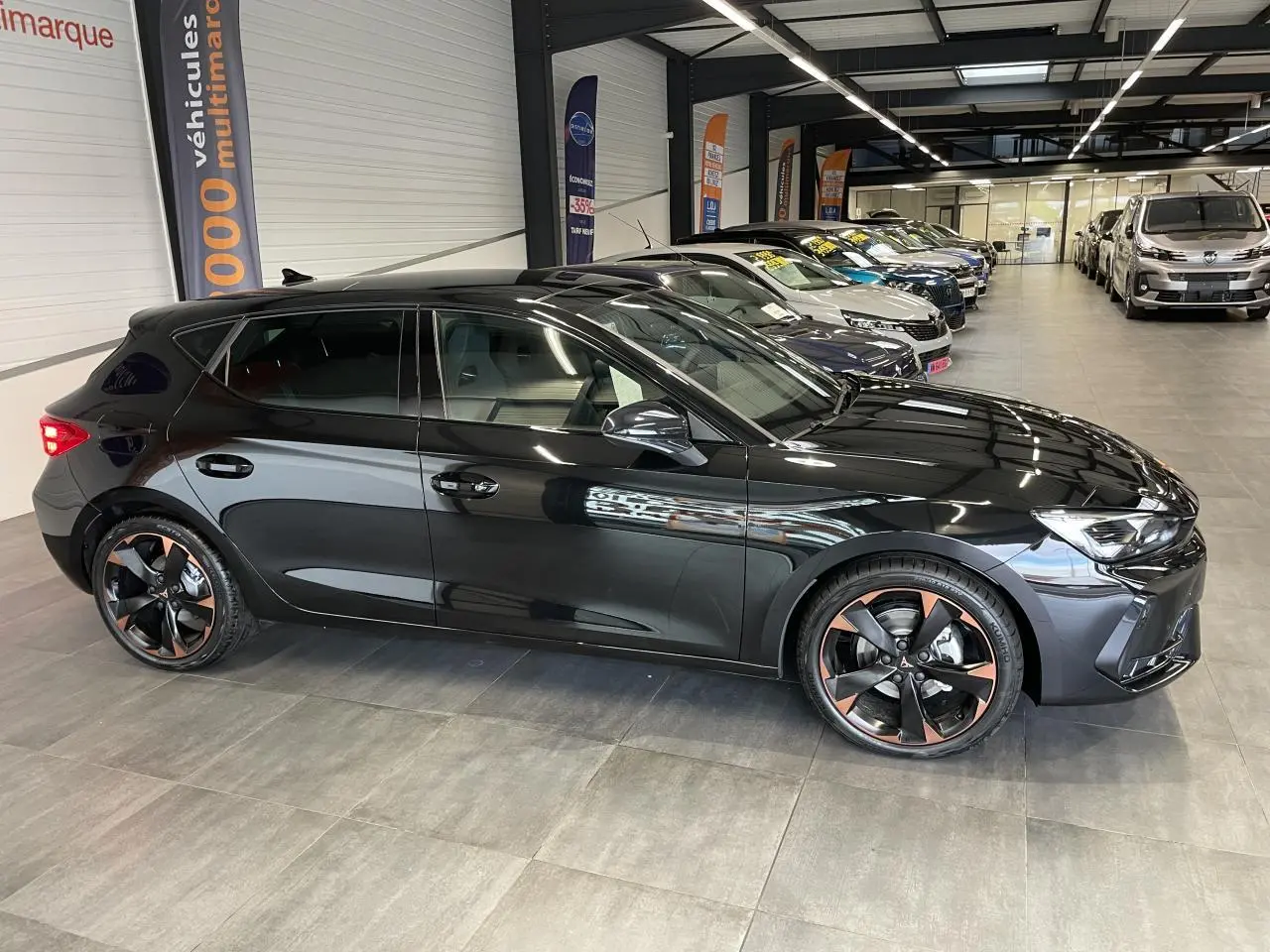 Vue de profil côté gauche d'une CUPRA Leon noire avec jantes alliage 18'' cuivrées en concession.