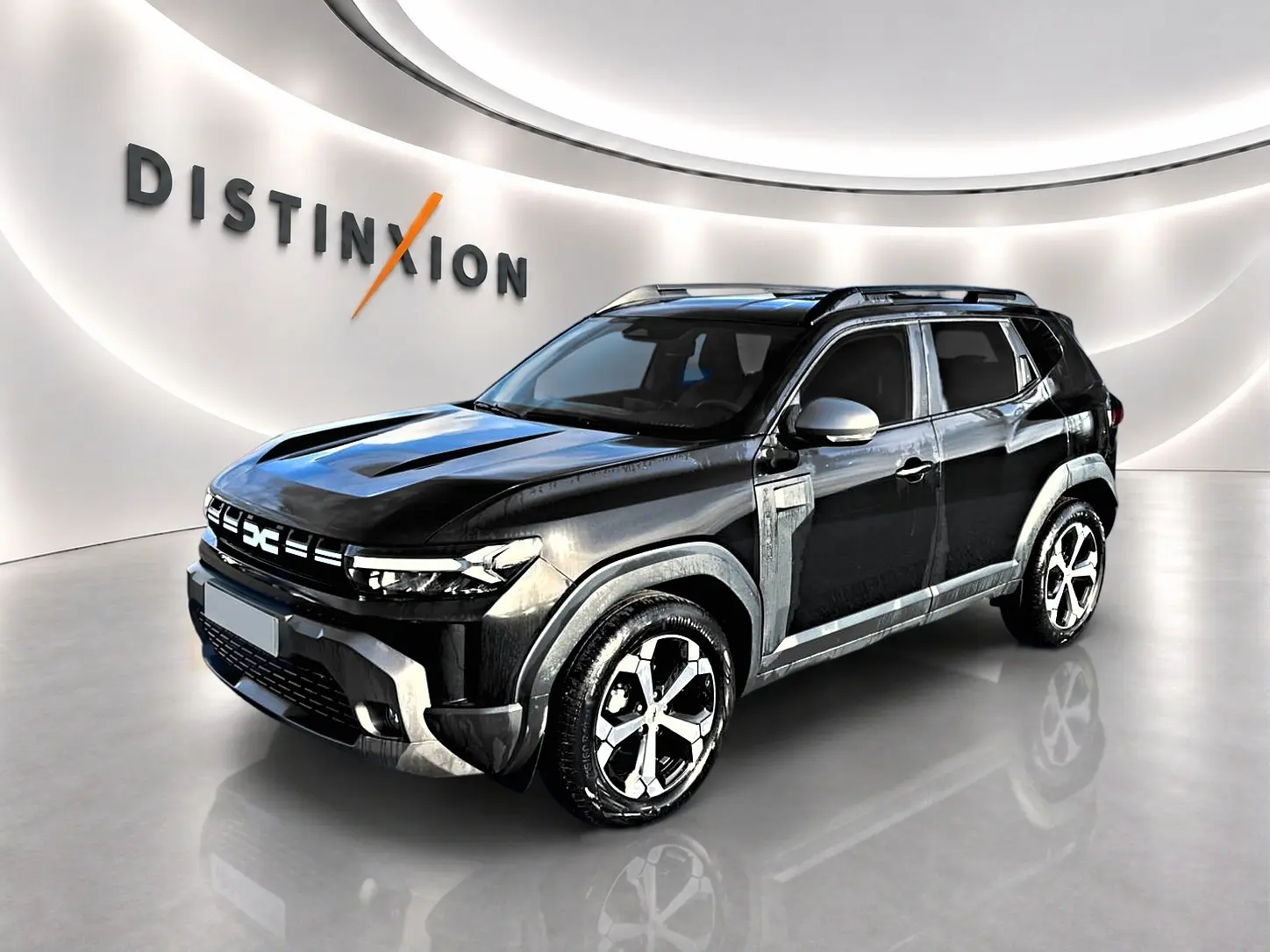 Dacia Duster noir en 3/4 avant droit, avec jantes alu distinctives et barres de toit visibles en showroom.