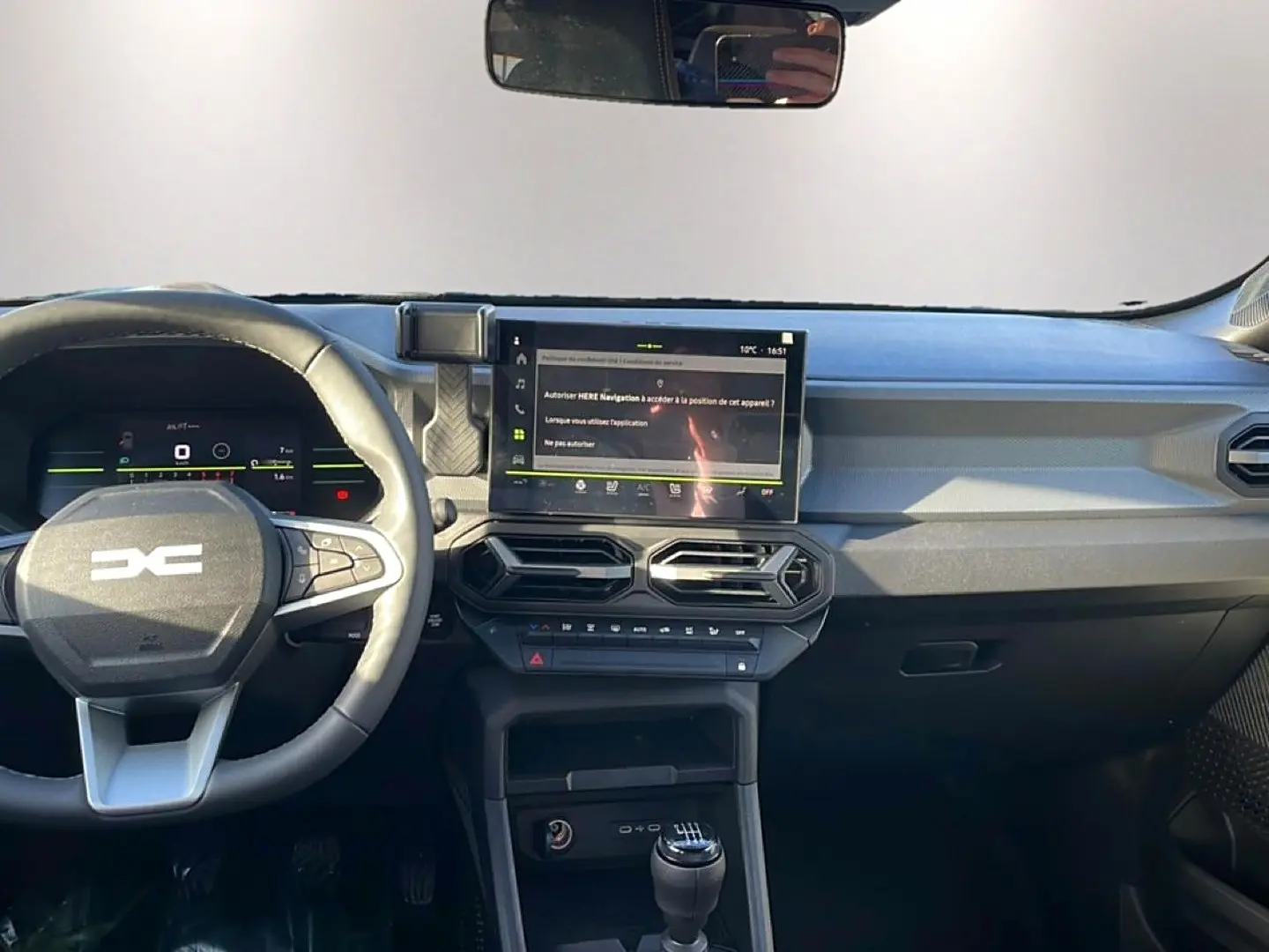 Vue intérieure du tableau de bord du Dacia Duster 2026 noir, avec volant multifonction, écran tactile et levier de vitesse manuel.