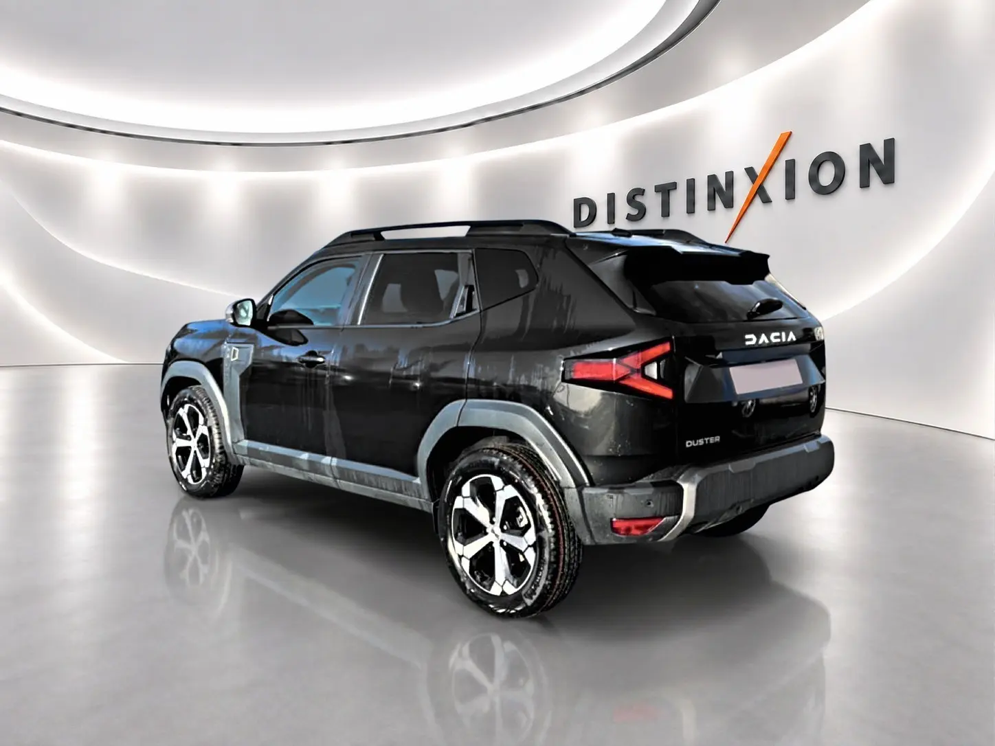 Dacia Duster noir vue 3/4 arrière droit en intérieur, avec jantes alu et barres de toit visibles.