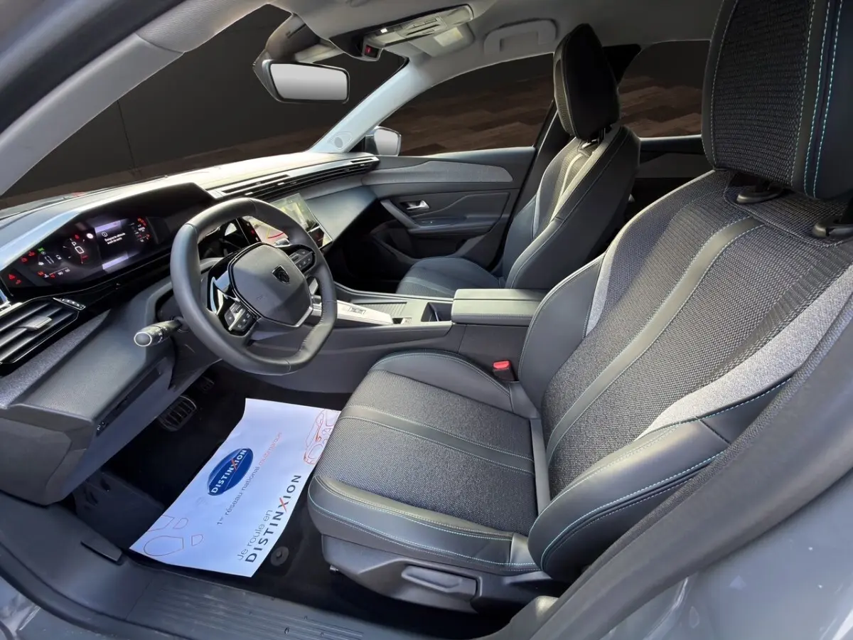 Vue intérieure côté conducteur de la Peugeot 308 Hybrid 145 e-DCS6 Allure 2025 avec sièges tissu et cuir gris foncé.