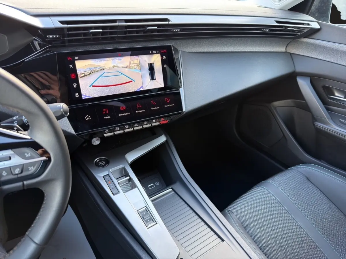 Intérieur de la Peugeot 308 Hybrid 145 e-DCS6 Allure 2025, vue côté passager avec écran tactile et console centrale grise.