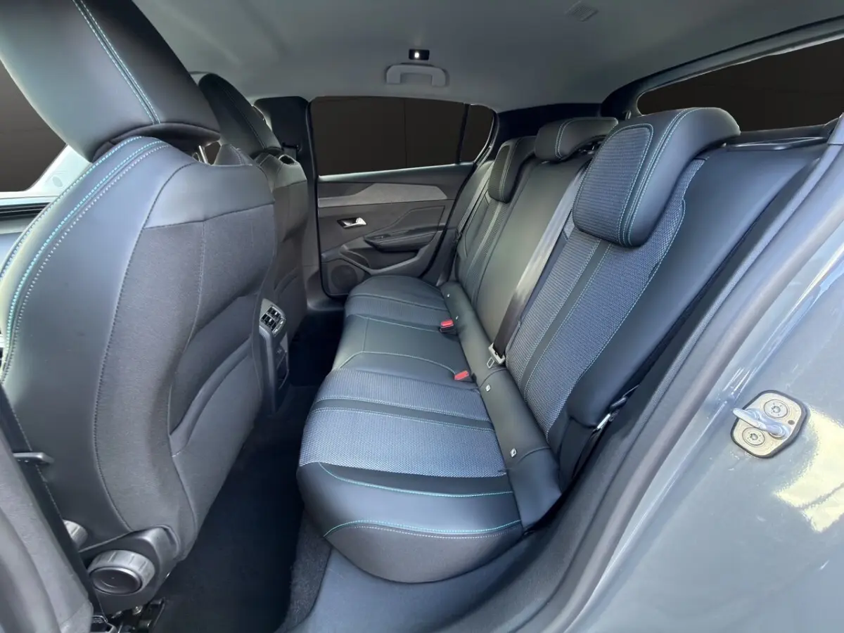 Vue latérale droite de l’arrière de la Peugeot 308 Hybrid gris foncé, montrant les sièges arrière en tissu et cuir avec surpiqûres bleues.