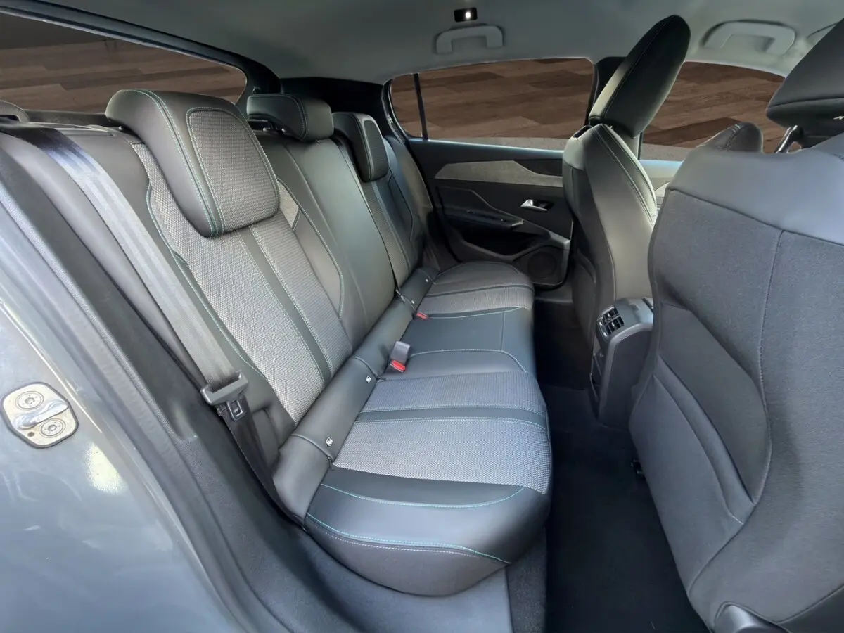 Vue intérieure arrière côté gauche de la Peugeot 308 Hybrid 145 Allure, sièges gris foncé en cuir et tissu avec surpiqûres bleues.