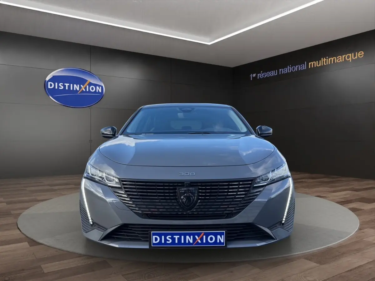Vue avant frontale de la Peugeot 308 Hybrid gris foncé avec calandre noire et feux LED verticaux allumés.