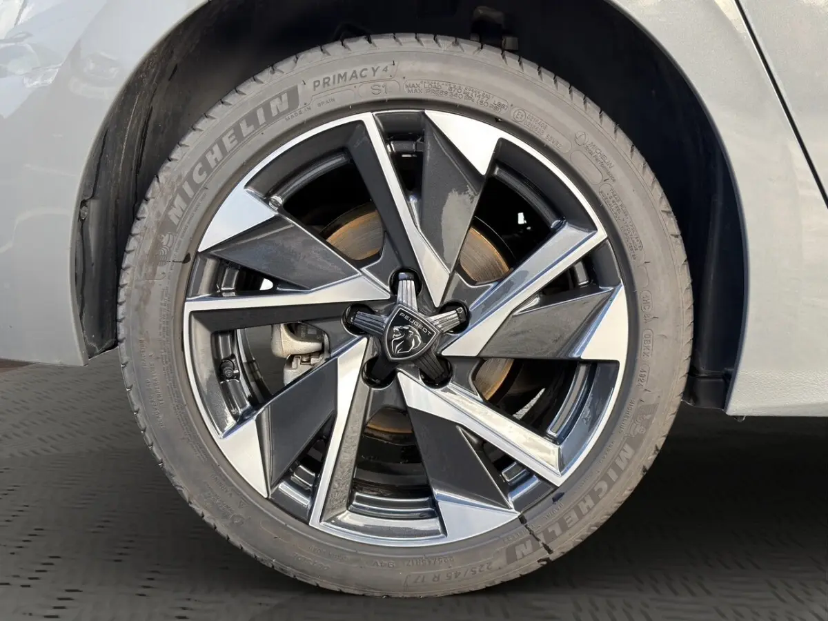 Gros plan sur la roue avant gauche de la Peugeot 308 Hybrid 145 e-DCS6 Allure gris foncé avec jante alliage bicolore et logo Peugeot.