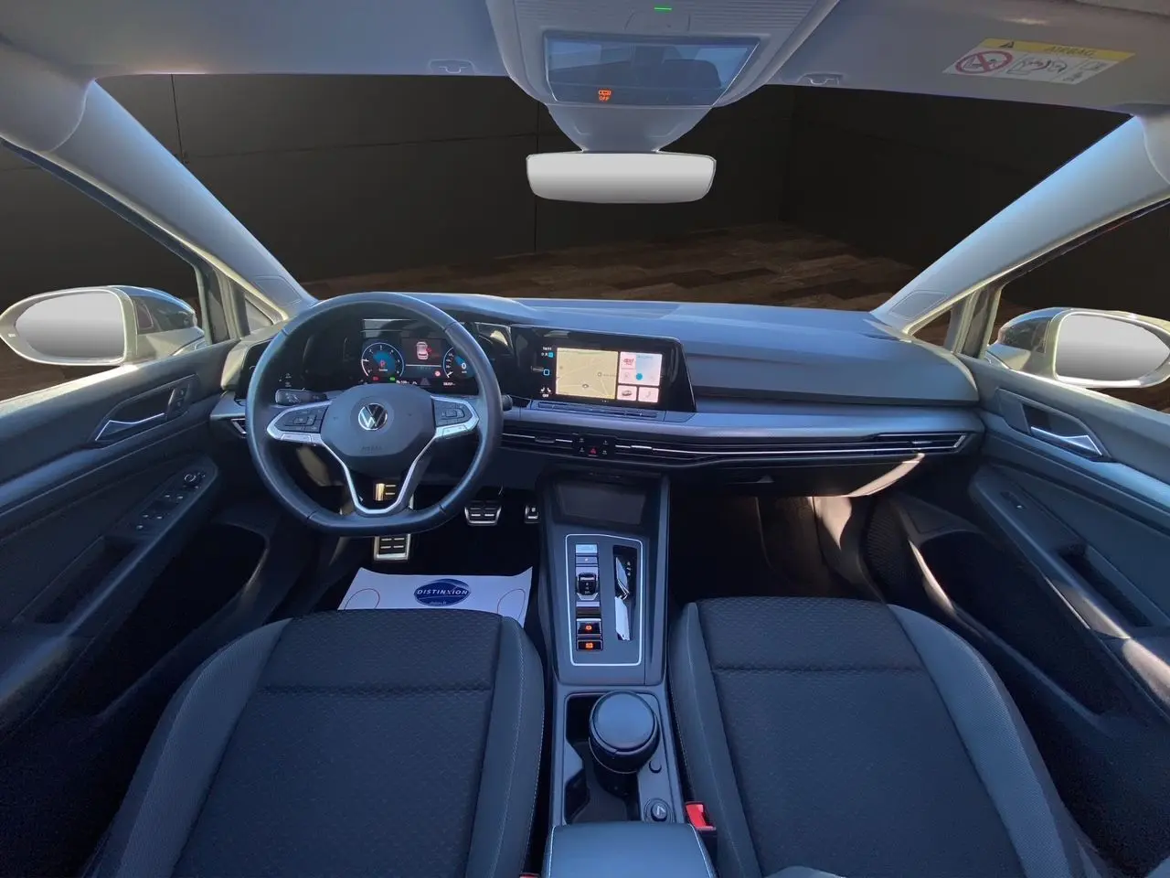 Vue intérieure avant de la Volkswagen Golf VIII noire, tableau de bord numérique et volant multifonction cuir visible.