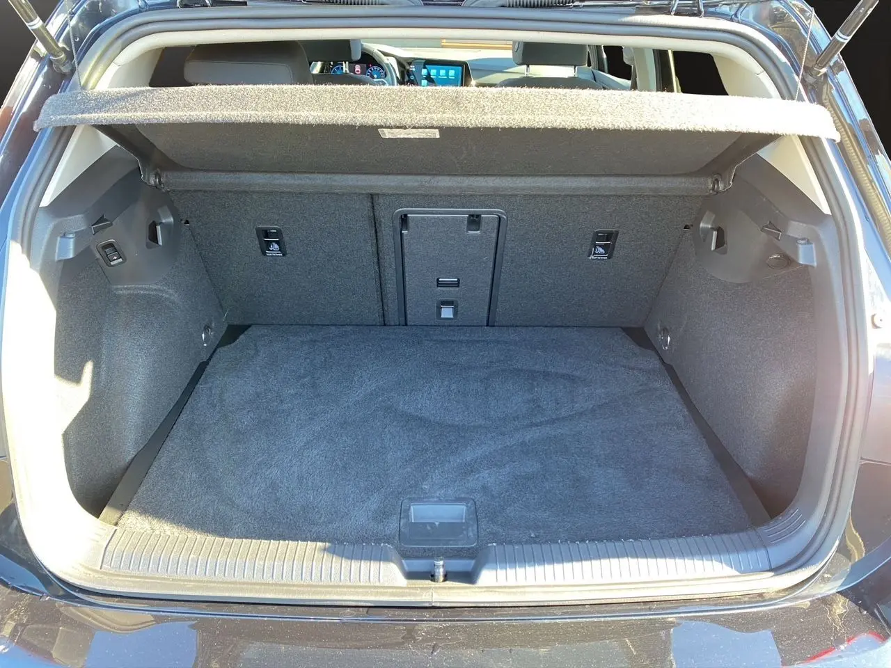 Coffre ouvert vu de l'arrière d'une Volkswagen Golf VIII noire, avec habillage intérieur gris et tablette de séparation.