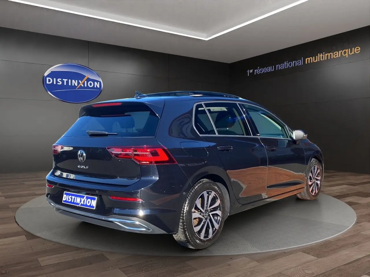 Vue 3/4 arrière droite d'une Volkswagen Golf VIII noire nacrée avec jantes alu et toit panoramique en showroom.