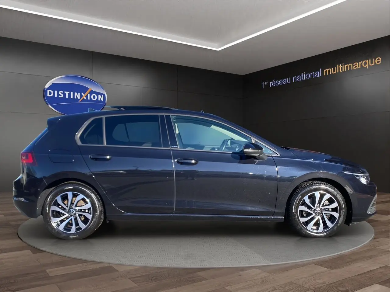 Vue de profil côté gauche d’une Volkswagen Golf VIII noire nacrée avec jantes alu 16 pouces dans un showroom.