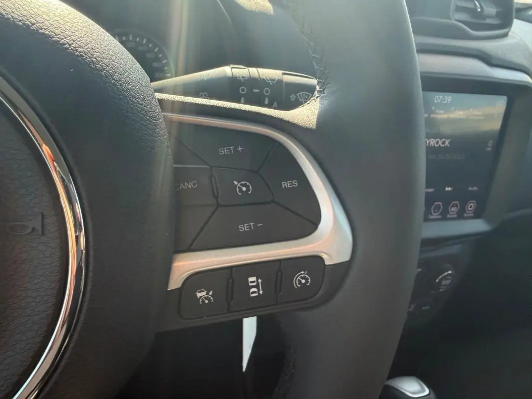 Gros plan sur le volant noir de la Jeep Renegade 2023, montrant les commandes du régulateur de vitesse et l'écran tactile en arrière-plan.