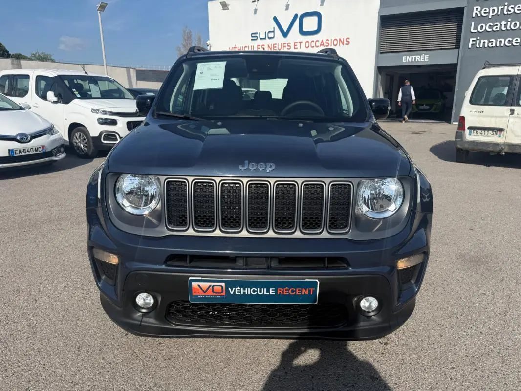 Vue frontale d'un Jeep Renegade bleu 2023 avec calandre à sept fentes et phares ronds, stationné devant un concessionnaire.
