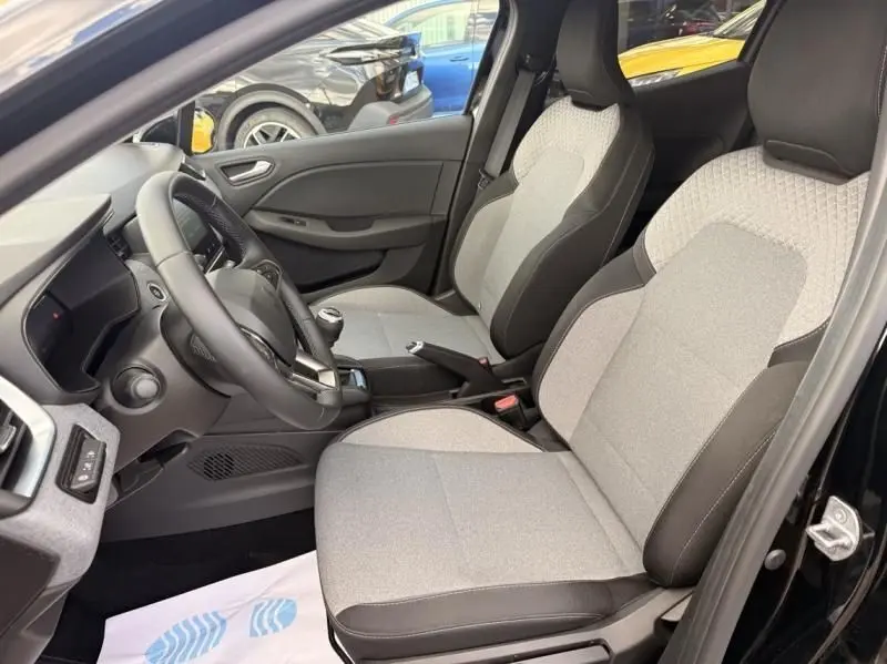 Vue intérieure côté conducteur de la Renault Clio V noire 2025, sièges tissu gris clair avec contours noirs et volant multifonction.
