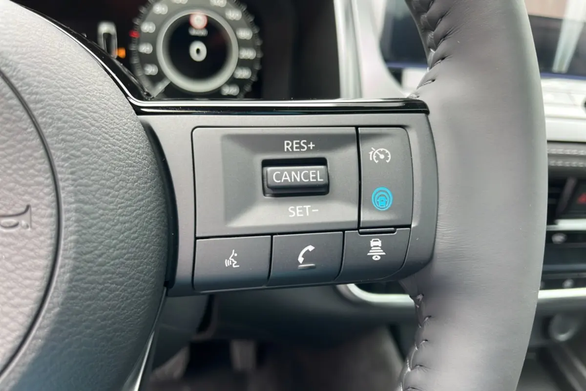 Gros plan sur les commandes au volant cuir gris du Nissan Qashqai E-POWER 205 Tekna Plus, avec tableau de bord flou en arrière-plan.