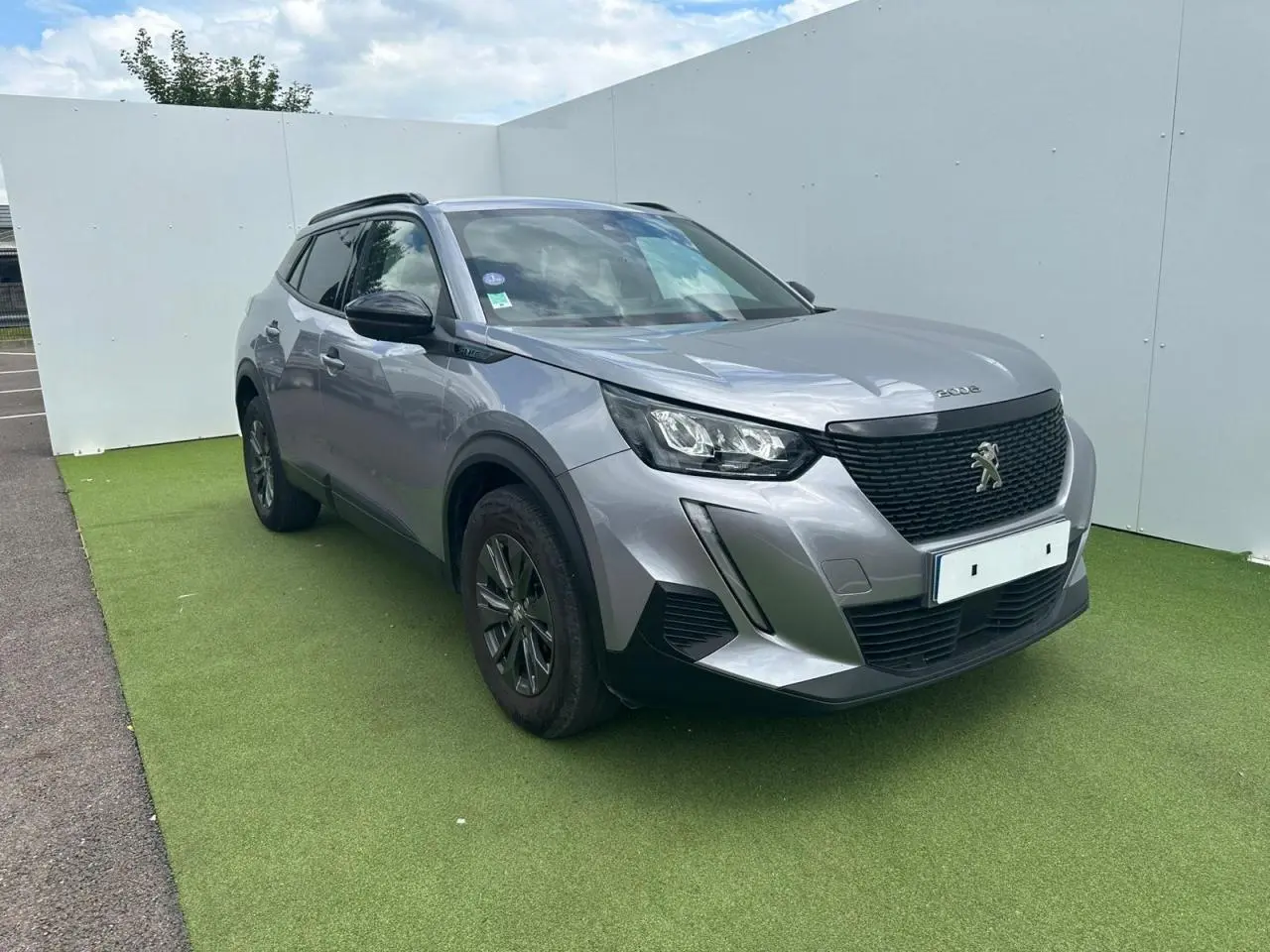 Peugeot 2008 gris clair en 3/4 avant droit, avec calandre noire et jantes alliage 16 pouces anthracite.