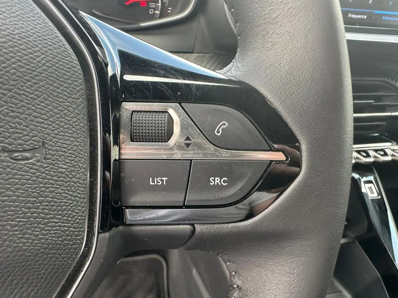 Gros plan sur les commandes multimédia noires à gauche du volant cuir du Peugeot 2008 gris clair 2022.