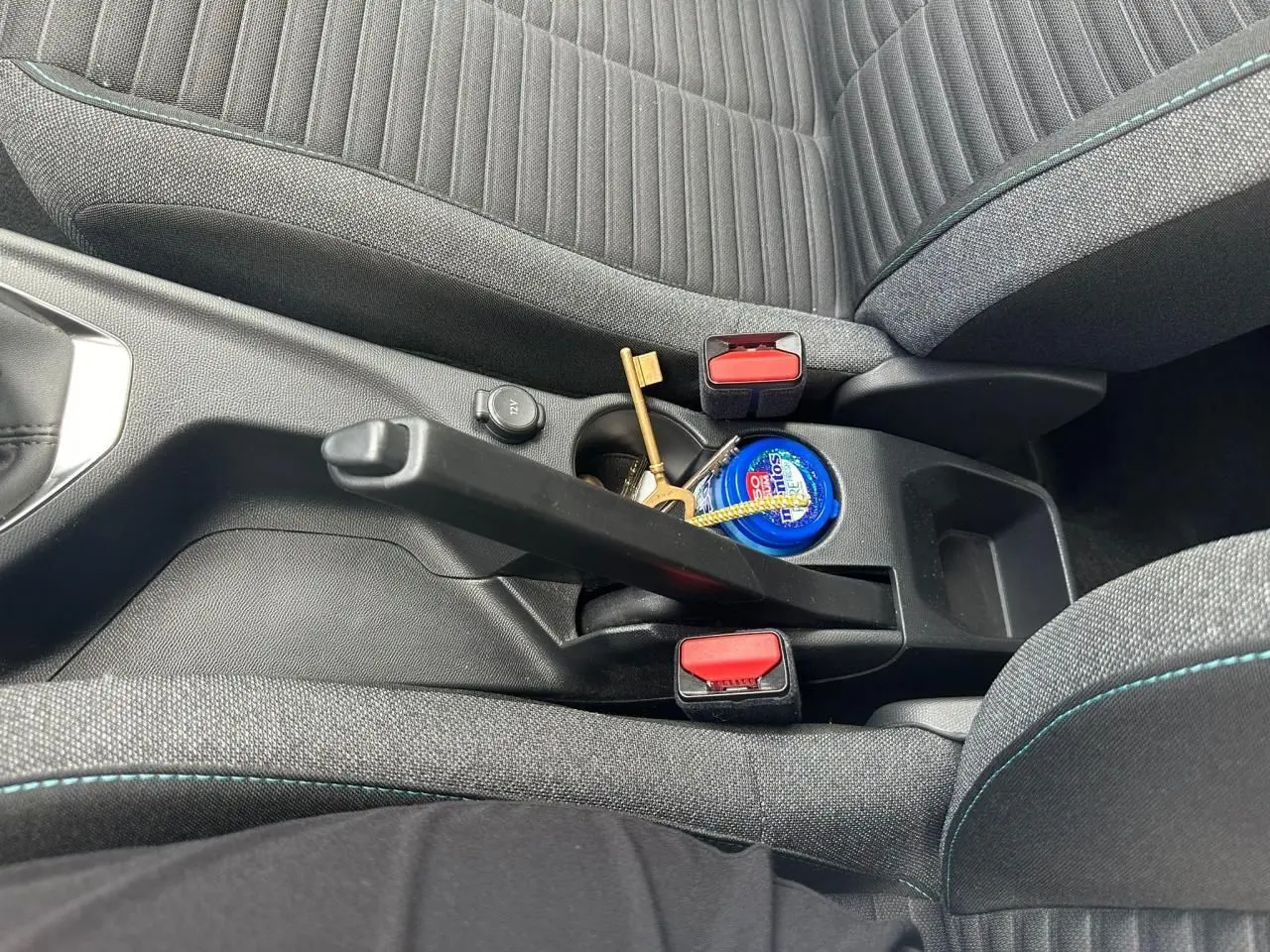 Gros plan sur la console centrale et frein à main d'un Peugeot 2008 II, sièges gris clair avec surpiqûres bleues.