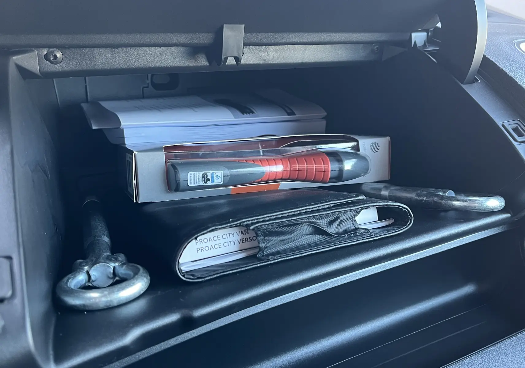 Intérieur du Toyota Proace City 2023 montrant la boîte à gants ouverte avec documents et outils rangés.