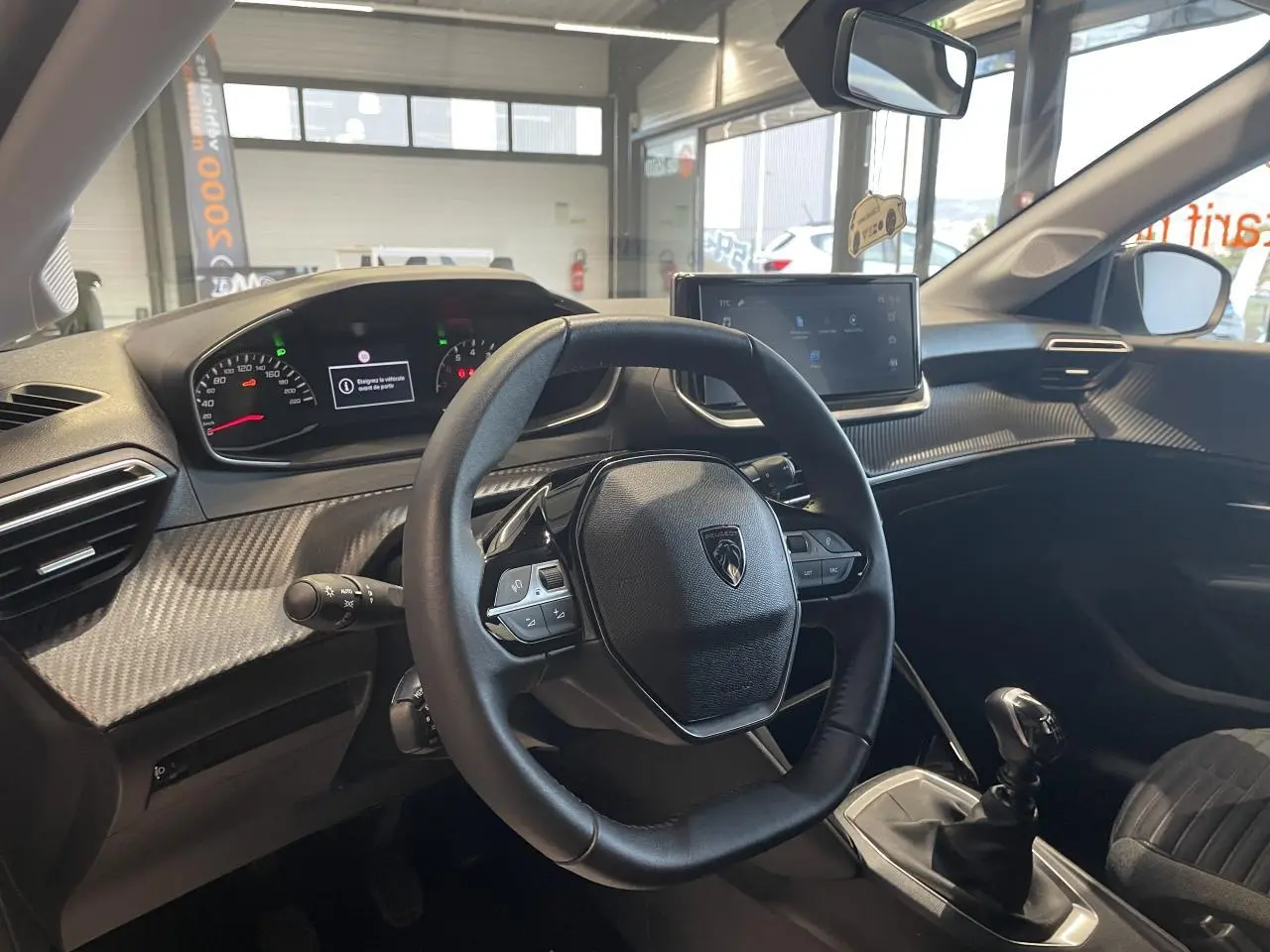 Intérieur de la Peugeot 208 2024 vue côté conducteur, volant cuir, tableau de bord et levier de vitesses manuelle.