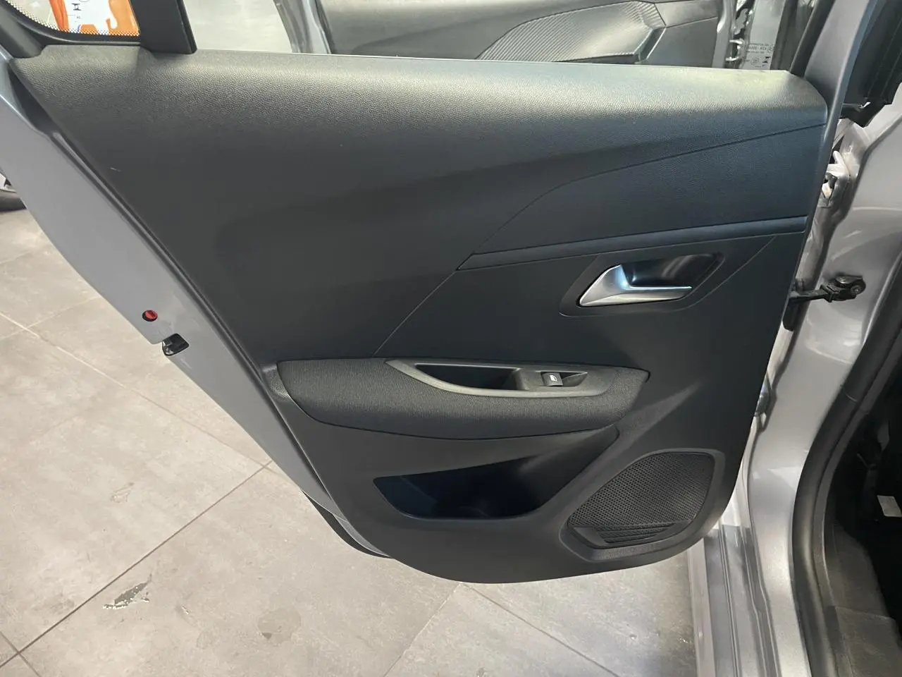 Vue intérieure côté gauche de la porte avant gris clair de la Peugeot 208 2024 avec panneau noir et haut-parleur intégré.
