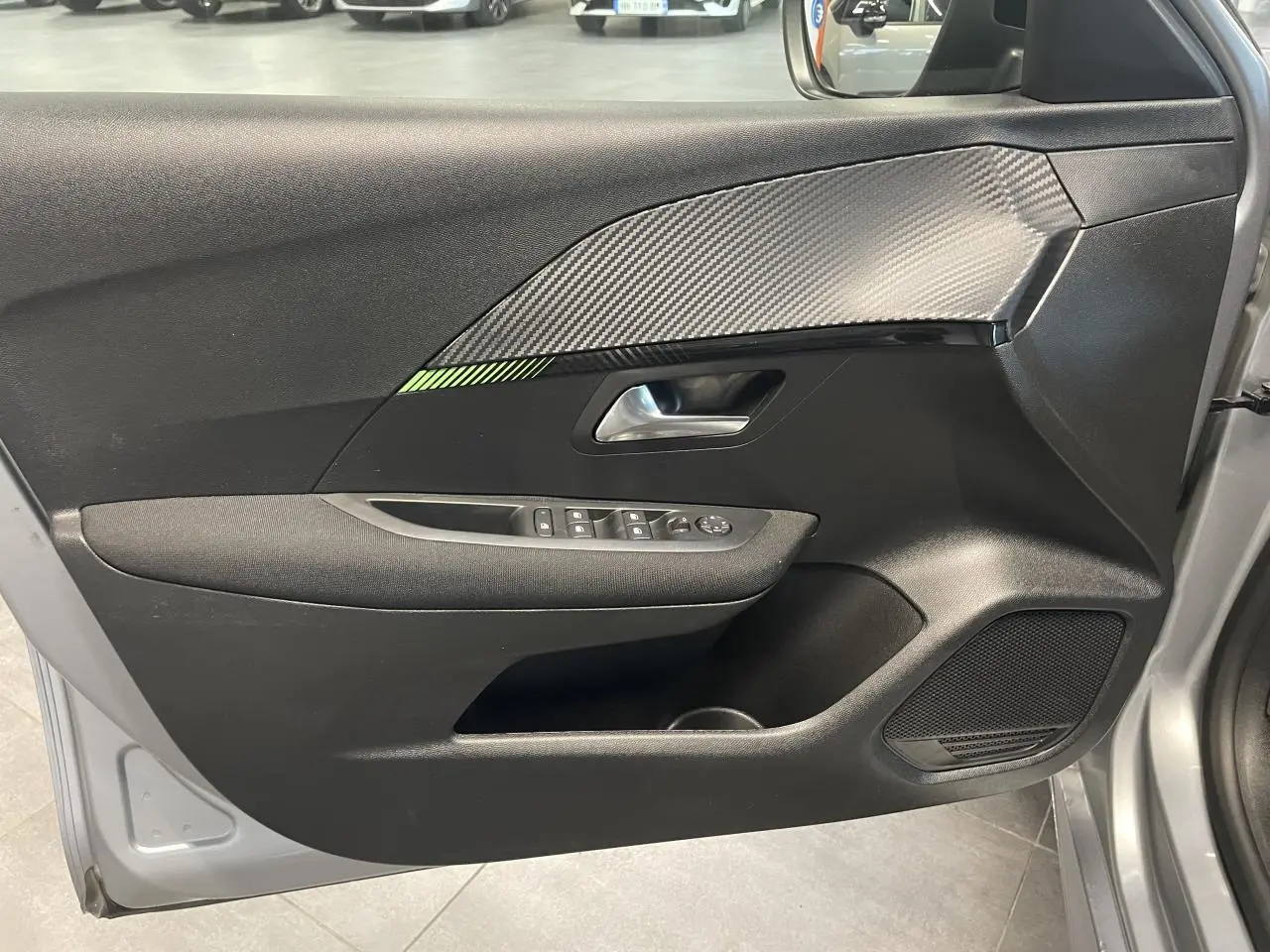 Porte avant gauche ouverte de Peugeot 208 gris clair, avec garniture noire et inserts carbone et vert.