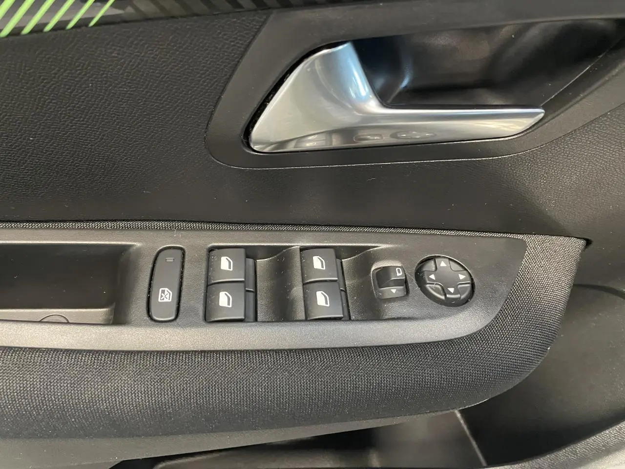 Détail des commandes de lève-vitres et réglage des rétroviseurs sur la porte avant gauche d'une Peugeot 208 gris clair 2024.