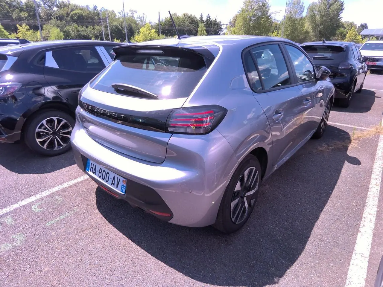 Vue 3/4 arrière droite d'une Peugeot 208 gris clair avec becquet noir brillant et feux arrière à LED en forme de griffes.