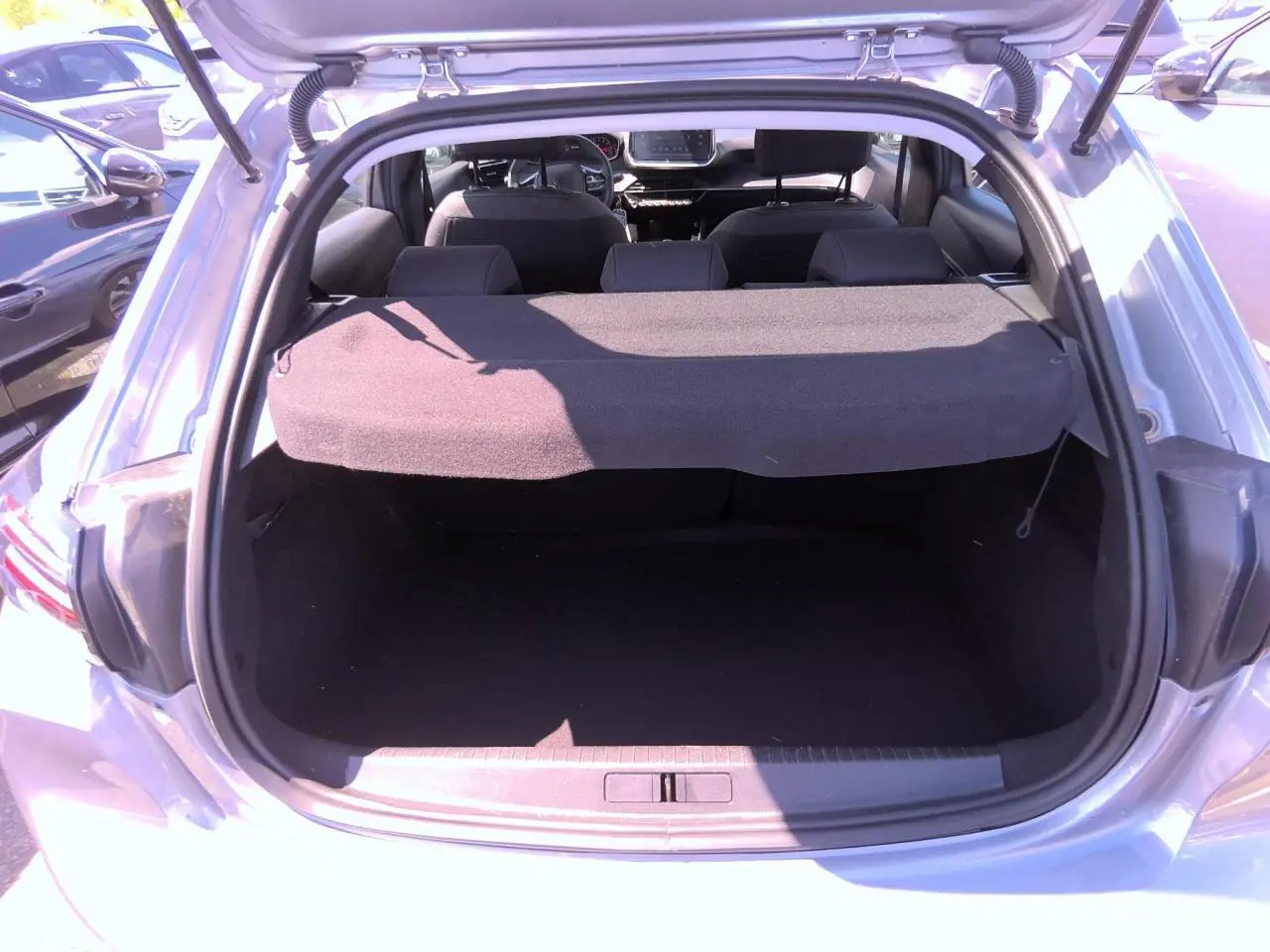 Coffre ouvert vu de l'arrière d'une Peugeot 208 gris clair, montrant l'intérieur et la plage arrière.