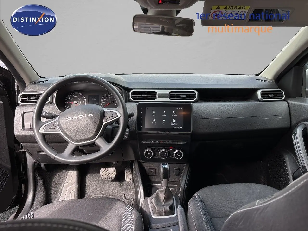 Vue intérieure avant du Dacia Duster 2024 noir, montrant le tableau de bord avec écran tactile et volant multifonction.
