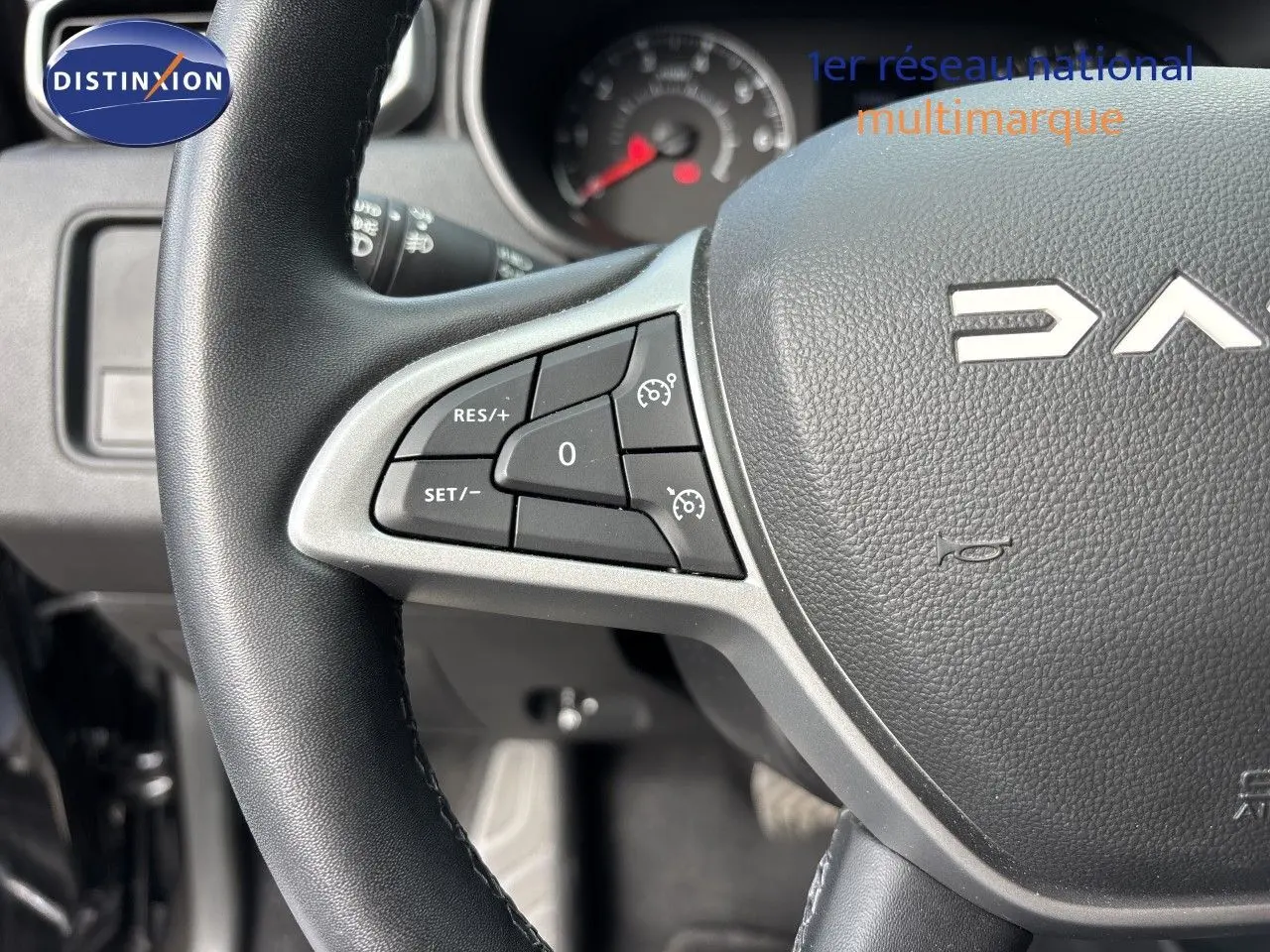 Gros plan sur le volant noir du Dacia Duster 2024 avec commandes de régulateur de vitesse visibles à gauche.