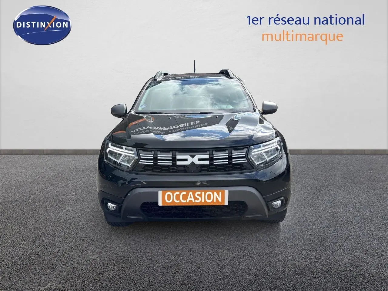 Vue frontale d'un Dacia Duster noir 2024 avec calandre distinctive et feux LED allumés sur fond neutre.