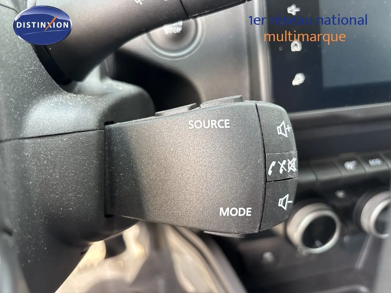 Gros plan sur la commande au volant du Dacia Duster noir 2024, avec boutons source, mode et contrôle audio visibles.