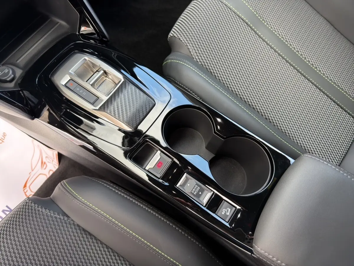 Vue rapprochée de la console centrale noire brillante avec levier de vitesses et sièges gris à surpiqûres vertes du Peugeot 2008 Hybrid 145.