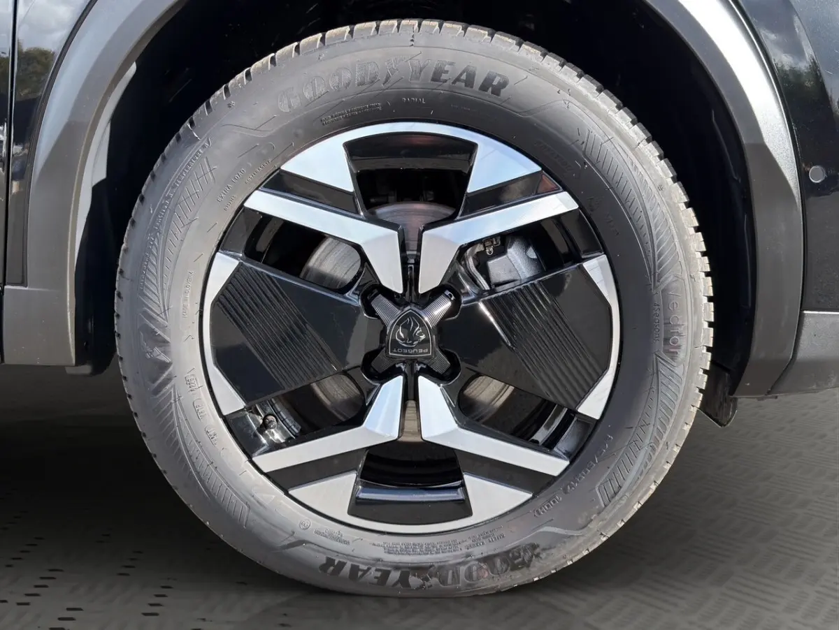 Gros plan sur la roue avant droite noire du Peugeot 2008 Hybrid 145 e-DCS6 GT avec jante alu bicolore et pneu Goodyear.