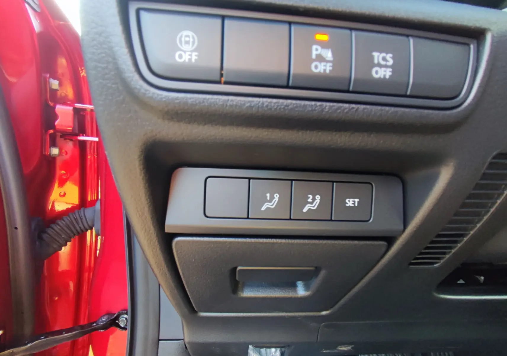 Gros plan sur les commandes de réglage des sièges et assistances au volant dans le rouge métallique Mazda MX-30 e-SKYACTIV 2023.