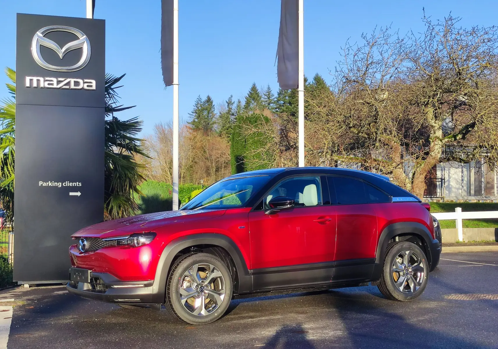 Vue latérale droite d'un Mazda MX-30 rouge métal 2023, soulignant ses jantes et son toit noir contrastant.