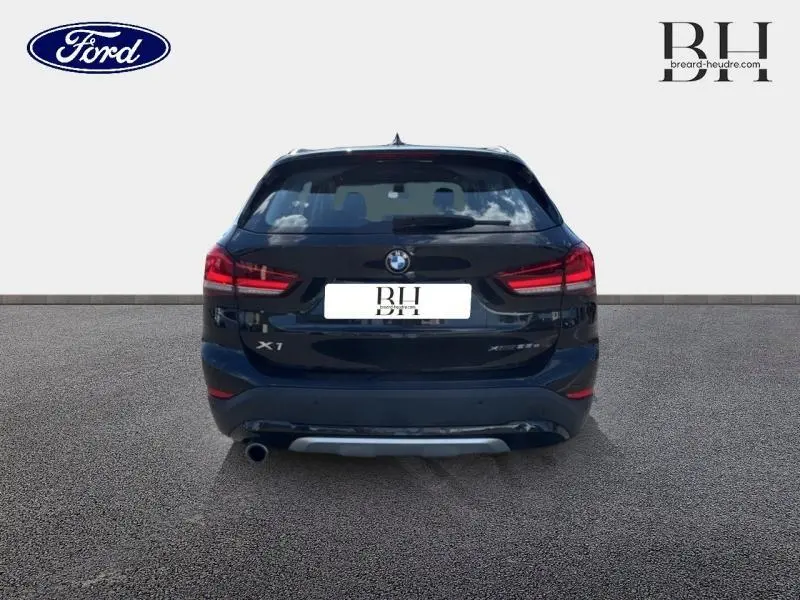 Vue arrière d'un BMW X1 xDrive25eA 220ch xLine 2021 en noir saphir avec feux arrière LED et sortie d'échappement chromée.