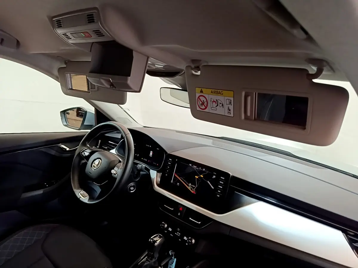 Intérieur du Skoda Kamiq 2022 vu côté conducteur, volant cuir et écran tactile de navigation allumé.