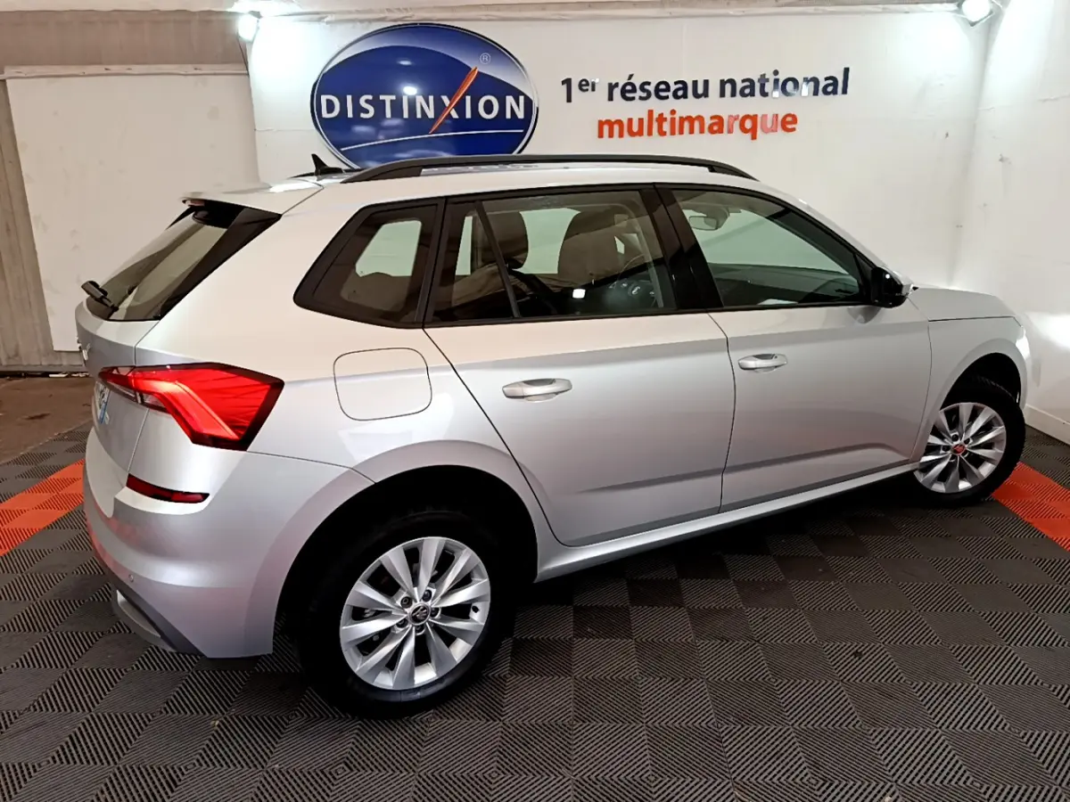 Vue 3/4 arrière droite d'un Skoda Kamiq gris clair 2022 avec jantes alliage et barres de toit noires.