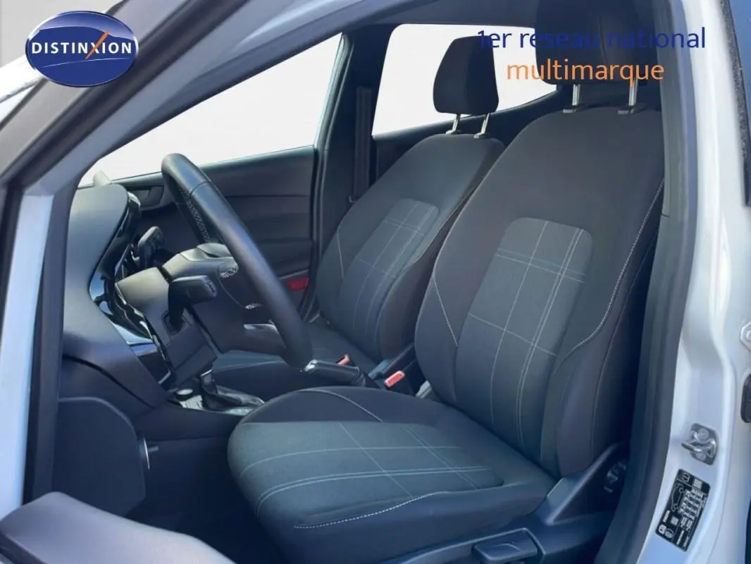 Vue intérieure côté conducteur de la Ford Fiesta blanche 2020, sièges tissu gris à motifs et tableau de bord moderne.