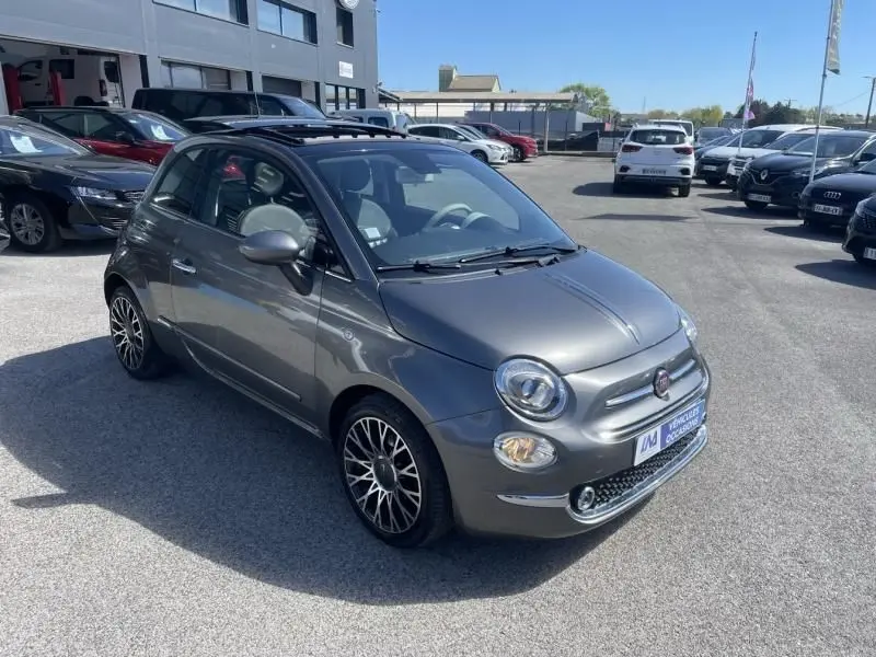 Vue 3/4 avant droite d'une FIAT 500 Club gris foncé de 2019 avec jantes alliage et toit ouvrant en concession.